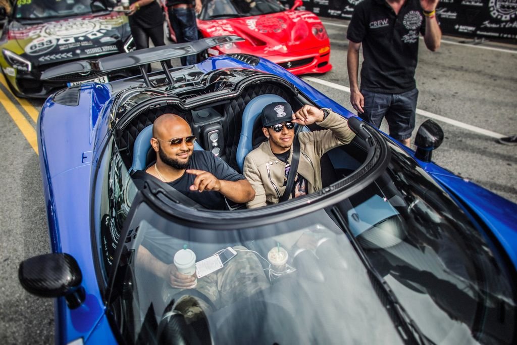 Lewis Hamilton saludando a los fans en el evento Gumball 3000, rodeado de supercoches y ambiente de lujo automovilístico | EUROPA COCHE